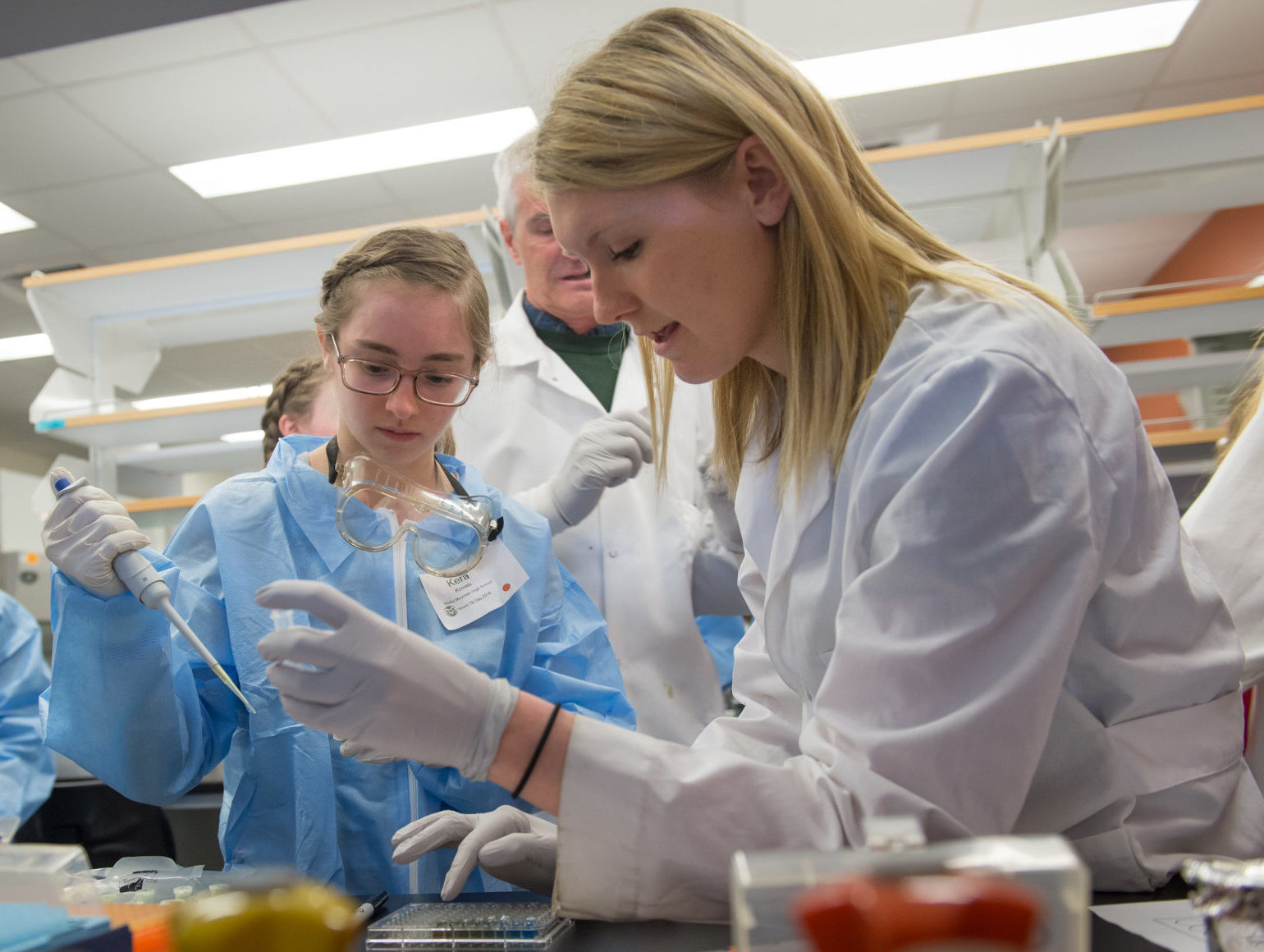Jessie Haugen Frenkel explains lab techniques to high school students in blue lab coats