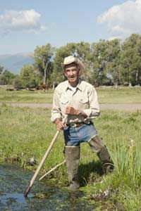man in hip waders holding a pole in some water