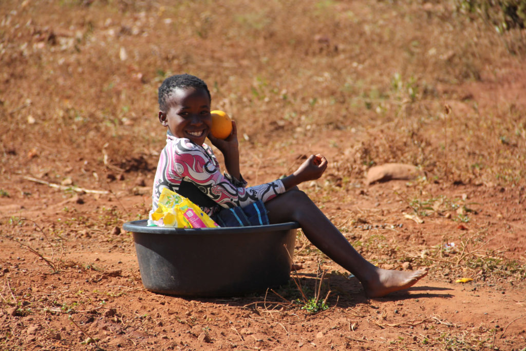 girl holding an orange while sitting in a basin